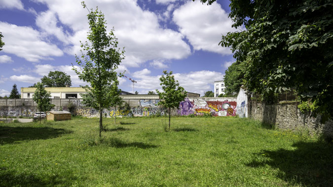 L’espace vert Simone Iff, d’une superficie conséquente d’environ 1 000m², comprend un grand arbre majestueux et de jeunes pousses récemment plantées. Il est délimité par des murs en pierre et un mur de clôture, la halle ne faisant pas partie du lieu à réinventer. Aujourd'hui, cet espace est sans usage, seul un composteur collectif a été installé. Au cœur du nouveau quartier Mitrie / Mellinet, il pourrait être propice aux rencontres et à la vie sociale.