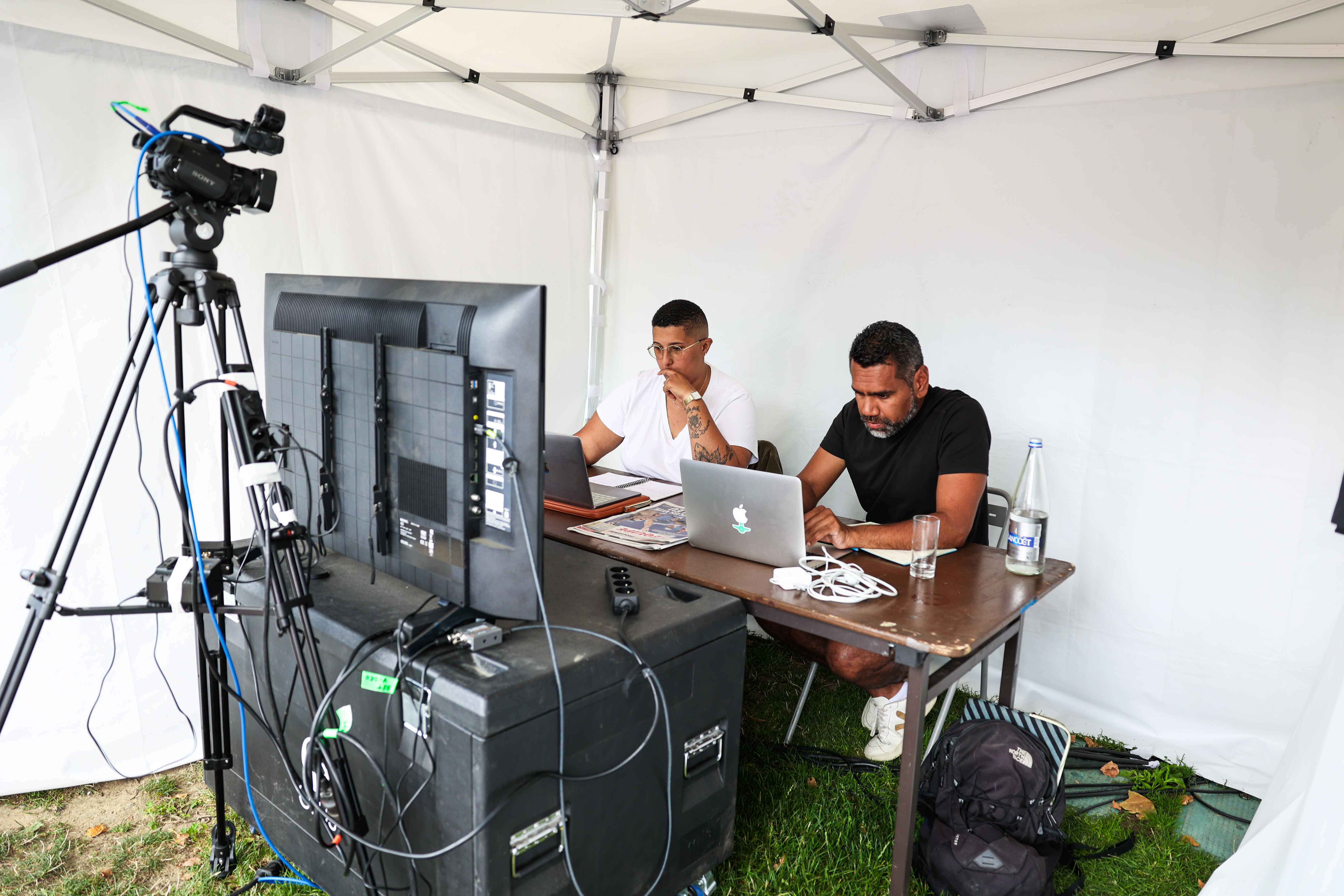 Photo montrant deux personnes, un homme et une femme, derrière un bureau ou figure de nombreux appareils informatiques, ils sont assis et filmés par une caméra fixe.