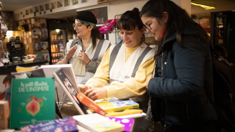 Deux jeunes femmes de l'association DisQtons proposent une sensibilisation autour de ressources type livres à un visiteur de passage.