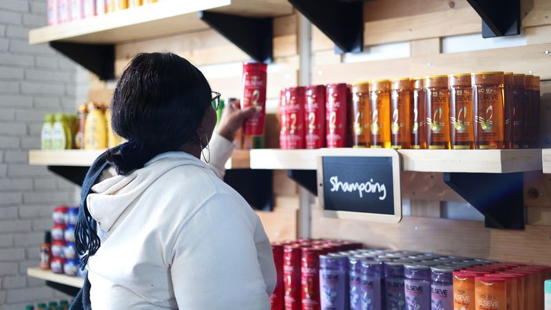 Photo d'une femme se saisissant d'un flacon de shampoing sur une étagère ou figure de nombreuses références de produits de beauté