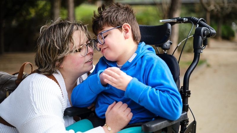 Femme faisant un calin à un enfant assis dans un fauteuil roulant