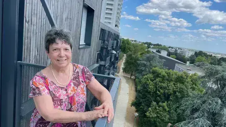 Une habitante appuyée à la rambarde de son balcon, dans un quartier rénové en 2025.