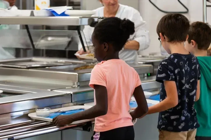 Des enfants patientent pour recevoir leurs plats à la cantine.