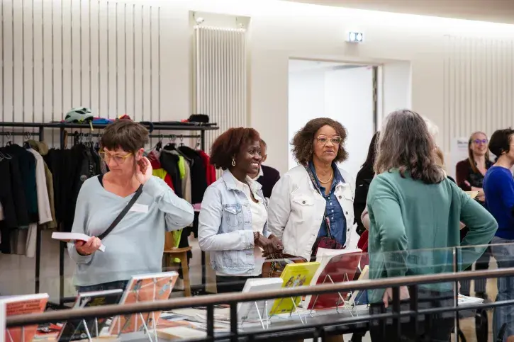 3 femmes se tiennent devant l'espace documentaire derrière lequel une femme seule se tien. Sur la table entre elles, de très nombreux livres et magazines. 